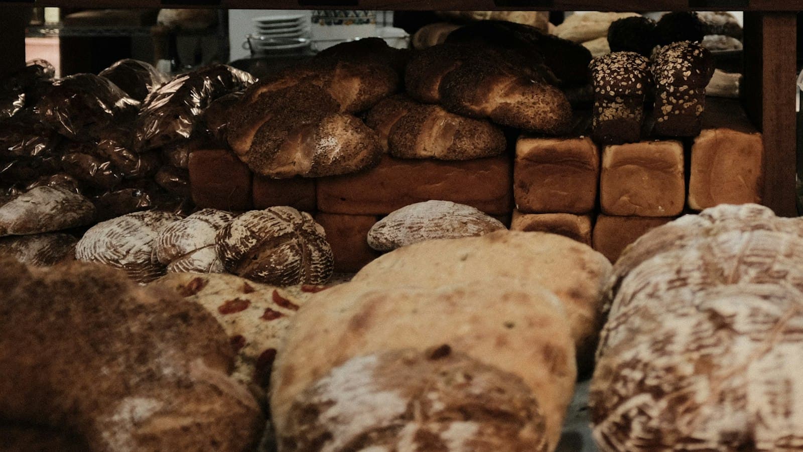 Półki piekarni zastawione bochenkami na zakwasie, chałkami z makiem i chlebami tostowymi w formach
