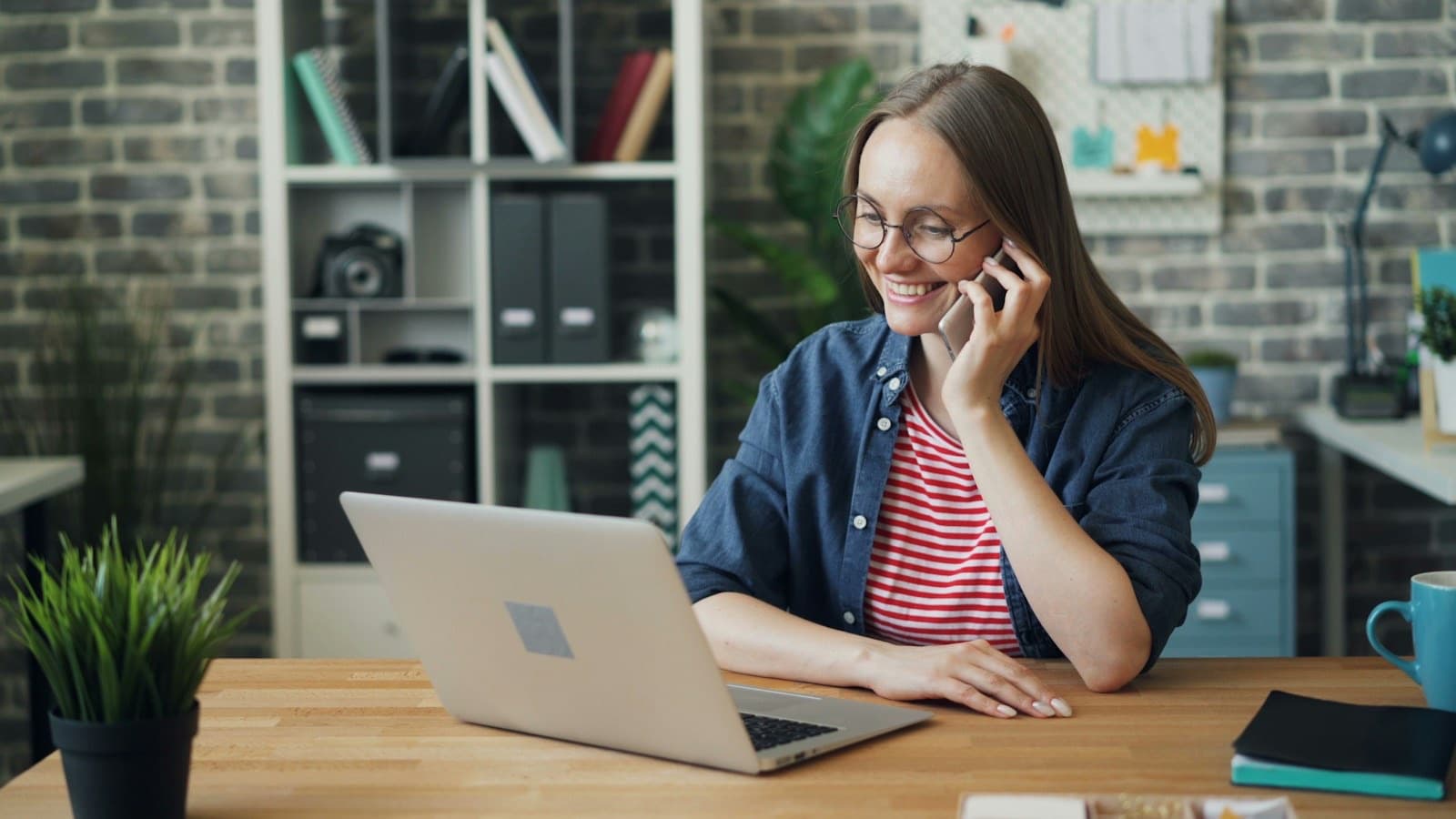 Uśmiechnięta kobieta rozmawia przez telefon przy biurku z laptopem - przyjmowanie zamówienia